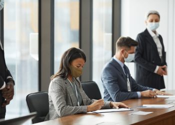 Professionals in face masks having a business meeting in a modern conference room.