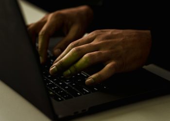 Crop anonymous person working on modern netbook and typing on keypad while surfing internet in dark room