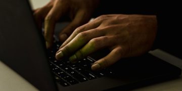 Crop anonymous person working on modern netbook and typing on keypad while surfing internet in dark room
