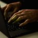 Crop anonymous person working on modern netbook and typing on keypad while surfing internet in dark room