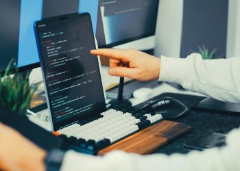 A programmer working on code with a laptop and monitor setup in an office.