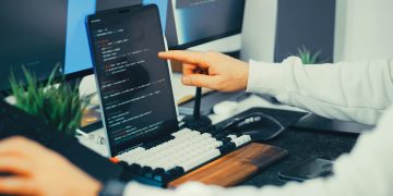 A programmer working on code with a laptop and monitor setup in an office.