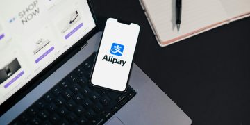 Smartphone displaying Alipay app on open laptop with online shopping site.