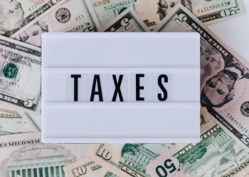 Top view of white vintage light box with TAXES inscription placed on stack of USA dollar bills on white surface