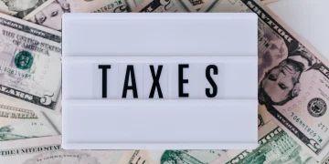 Top view of white vintage light box with TAXES inscription placed on stack of USA dollar bills on white surface