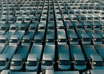 Overhead shot of a large collection of white pickup trucks parked in neat rows, emphasizing industrial scale.
