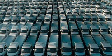 Overhead shot of a large collection of white pickup trucks parked in neat rows, emphasizing industrial scale.