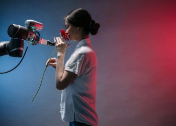 A woman in a lab coat interacts with a robot arm holding a red flower, symbolizing technology and nature.