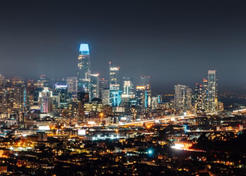 Illuminated city with high rise buildings and skyscrapers on street with busy road at night