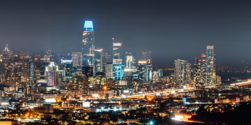 Illuminated city with high rise buildings and skyscrapers on street with busy road at night
