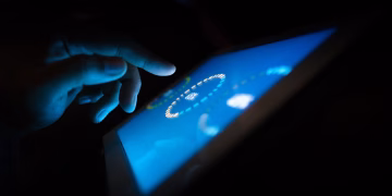 Close-up of a hand interacting with a glowing touchscreen in a dark setting, highlighting technology use.