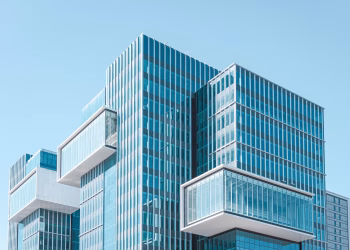 Striking contemporary glass building with unique geometric extensions under clear blue sky.