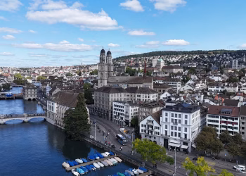 Aerial cityscape of Zurich, showcasing historic architecture, river, and Limmatquai under a vibrant blue sky.