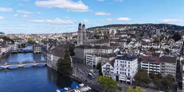 Aerial cityscape of Zurich, showcasing historic architecture, river, and Limmatquai under a vibrant blue sky.