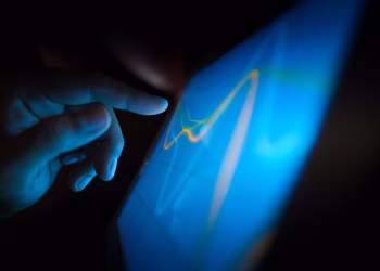 Close-up of a hand interacting with a touchscreen displaying dynamic graphs.