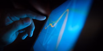 Close-up of a hand interacting with a touchscreen displaying dynamic graphs.