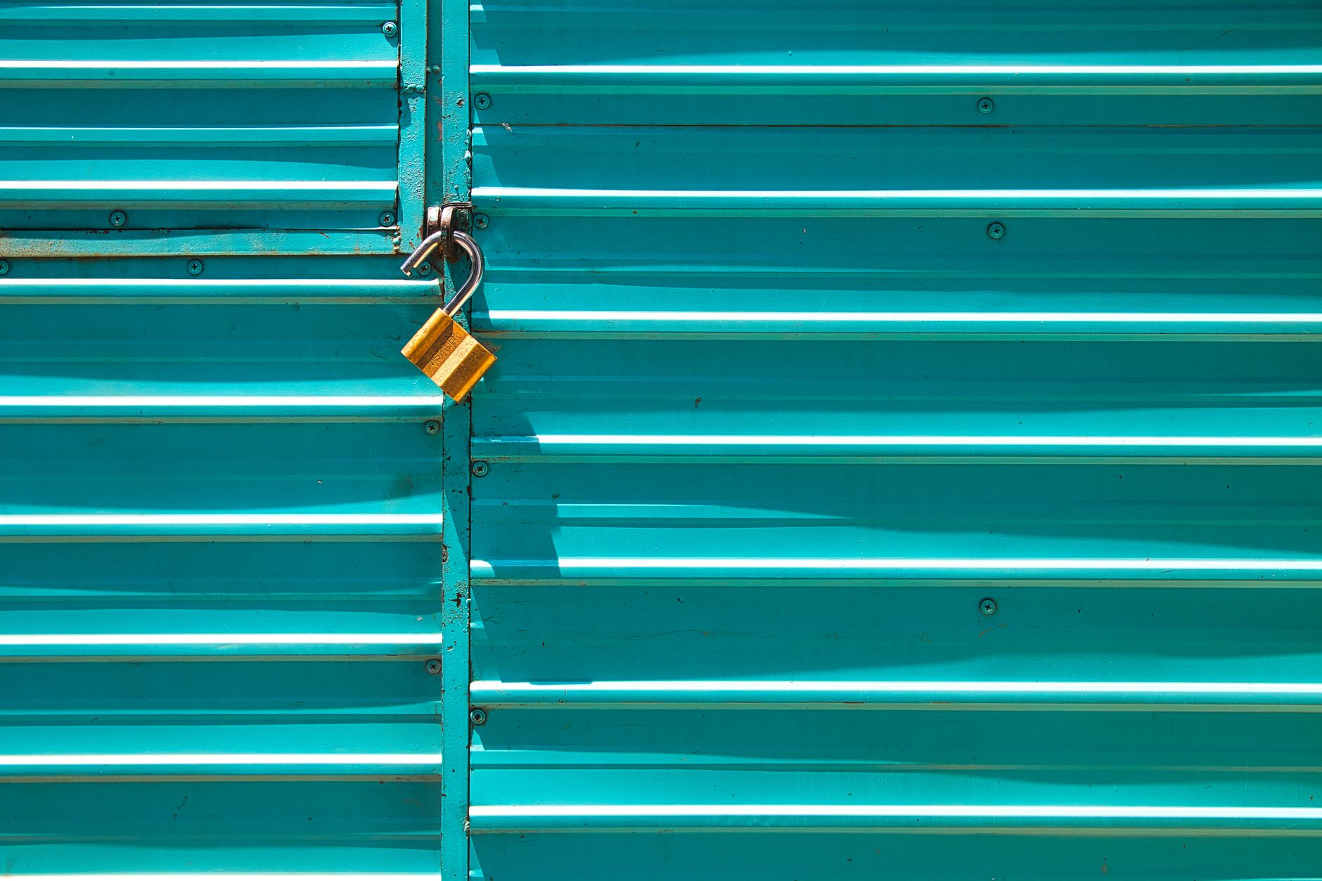 Close-up of a turquoise metal door with a golden padlock, emphasizing security.