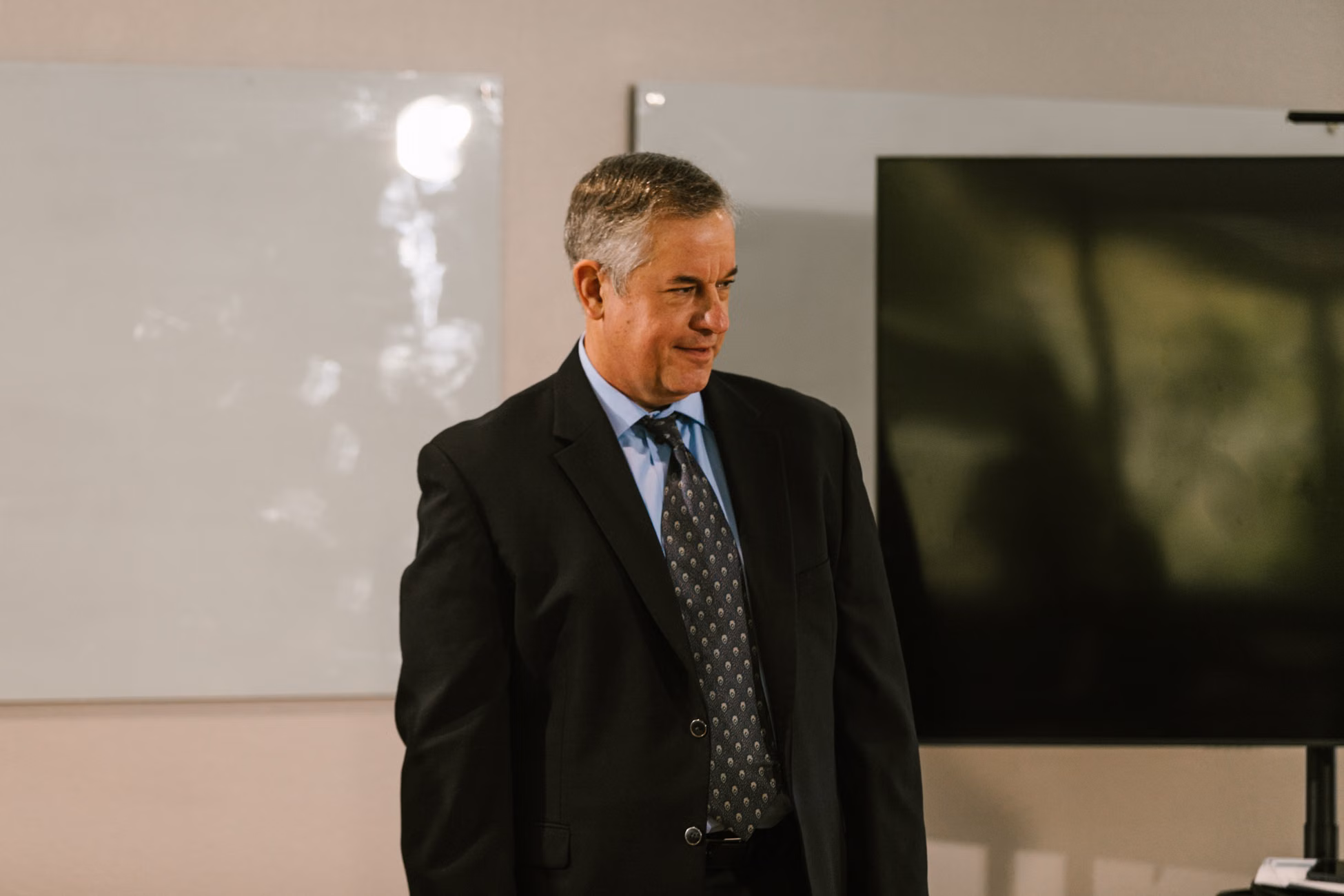 Senior man in a suit standing indoors, signifying a professional corporate setting.