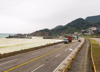 Trucks traveling on a coastal road with beautiful mountain and ocean views, enhancing logistics imagery.