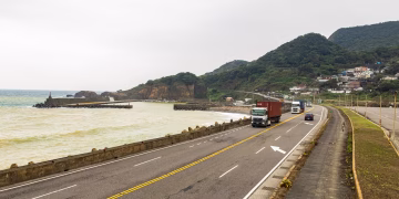 Trucks traveling on a coastal road with beautiful mountain and ocean views, enhancing logistics imagery.