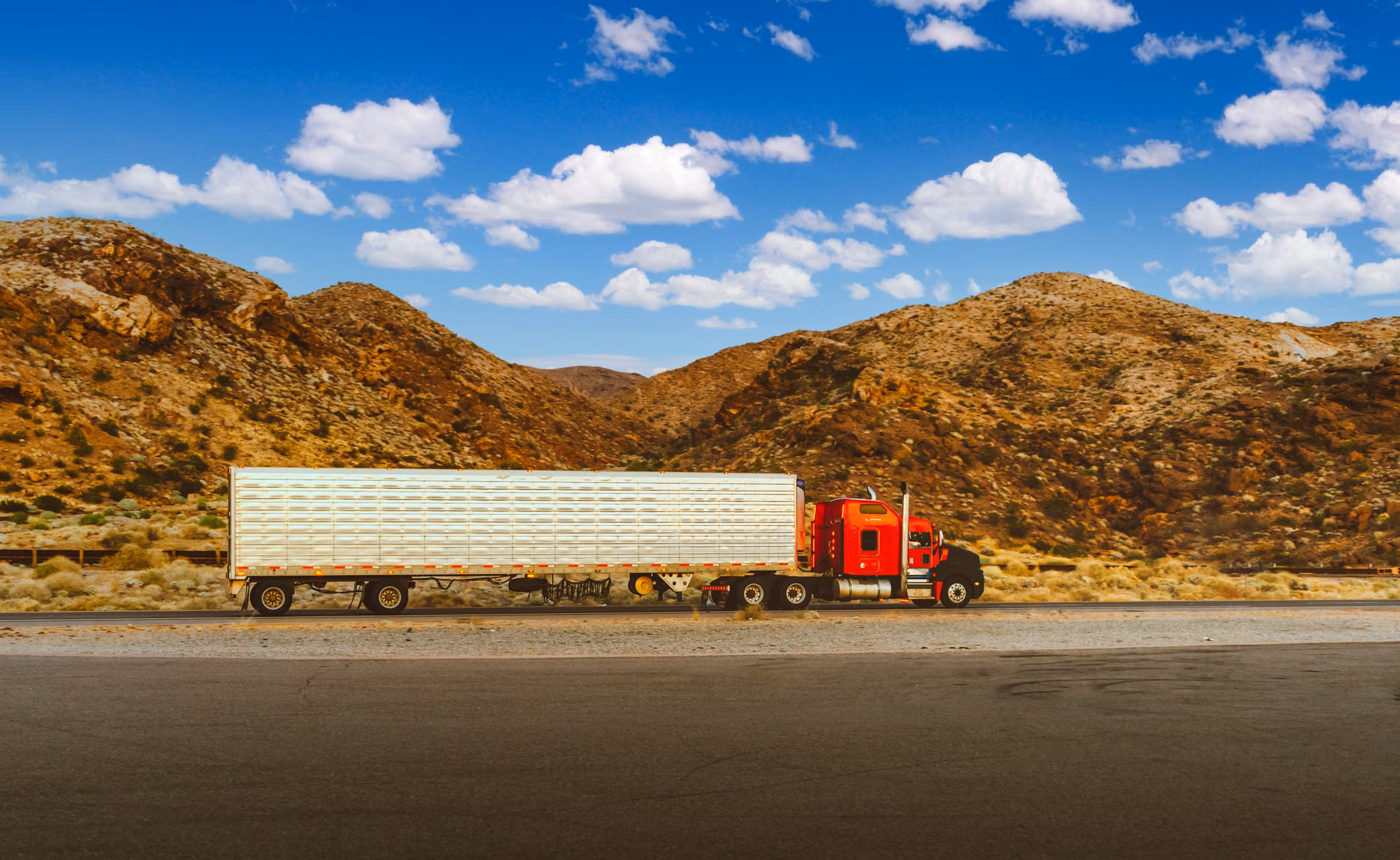 A vibrant red semi-truck travels through a desert highway with mountain views in Nevada.