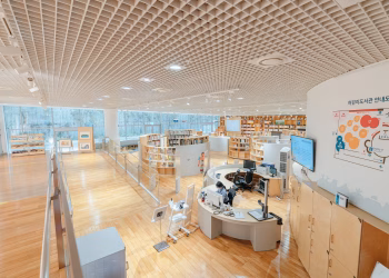 Open and airy modern library with bookshelves, desks, and a large screen in a well-lit space.