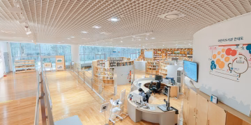 Open and airy modern library with bookshelves, desks, and a large screen in a well-lit space.