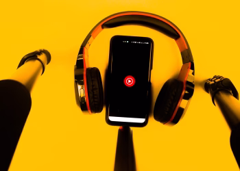A smartphone with wireless headphones and microphone set against a vibrant yellow background.