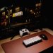 Close-up of a gaming desk setup featuring a keyboard, controller, and monitor at night.