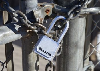 Detailed view of a padlock securing a metal gate with a chain, emphasizing safety and security.