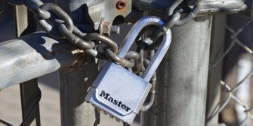 Detailed view of a padlock securing a metal gate with a chain, emphasizing safety and security.