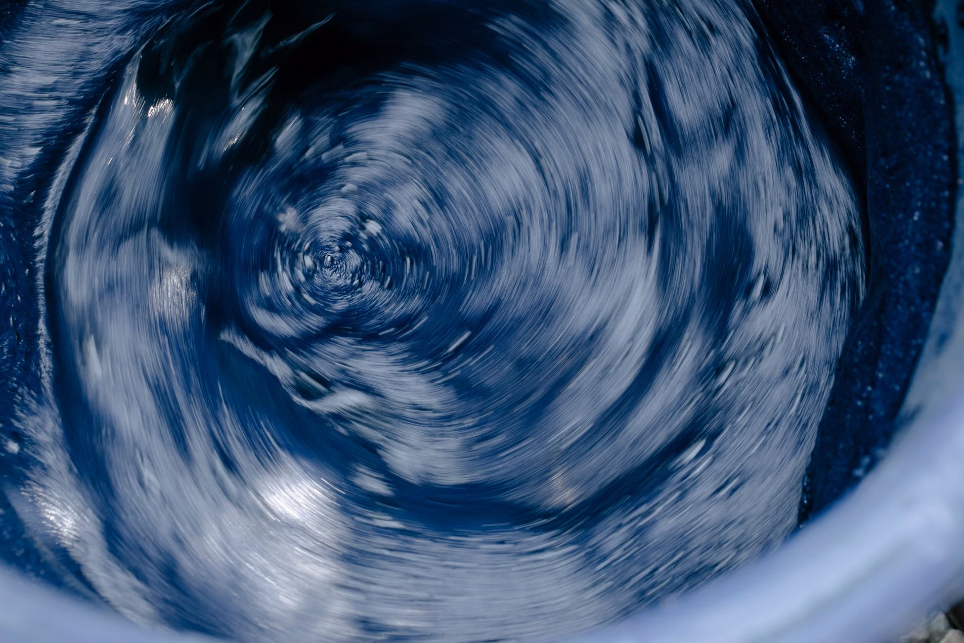 Abstract background of blue colored swirling water in washing machine in motion in daylight