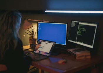 Woman using multiple screens for cybersecurity tasks in a cozy home office