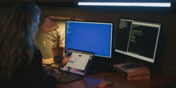 Woman using multiple screens for cybersecurity tasks in a cozy home office