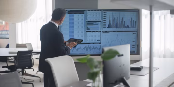 Professional in suit analyzing financial data on screens in a modern office setting.