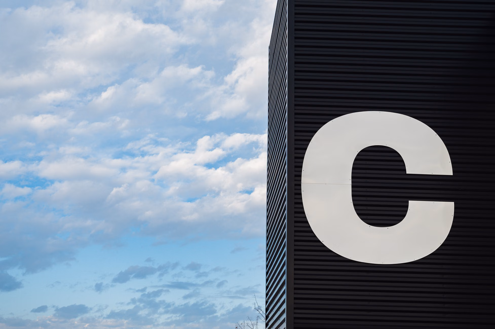 A modern facade featuring a large letter C against a vibrant sky with clouds.