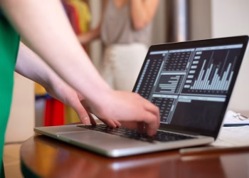 Hands typing on a laptop displaying data charts in an indoor setting.