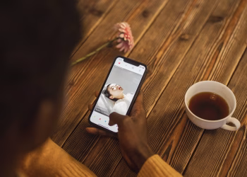 An individual using a dating app on a smartphone with a cup of tea nearby on a wooden table.