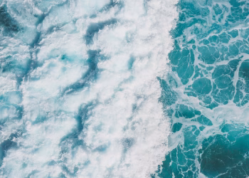 Aerial view of vibrant turquoise ocean waves creating white sea foam and splashes.