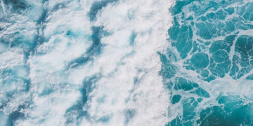 Aerial view of vibrant turquoise ocean waves creating white sea foam and splashes.