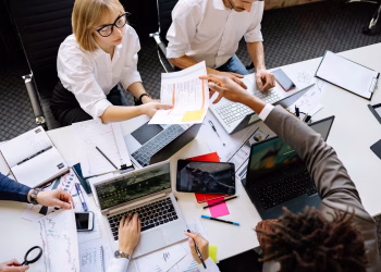 Diverse team collaborating in a modern office with laptops and documents.
