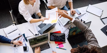 Diverse team collaborating in a modern office with laptops and documents.