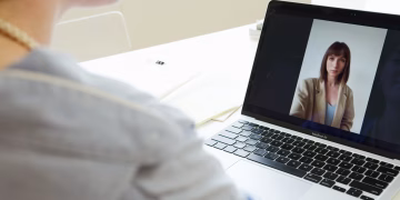 Close-up of woman on a video call using a laptop in a modern workspace.