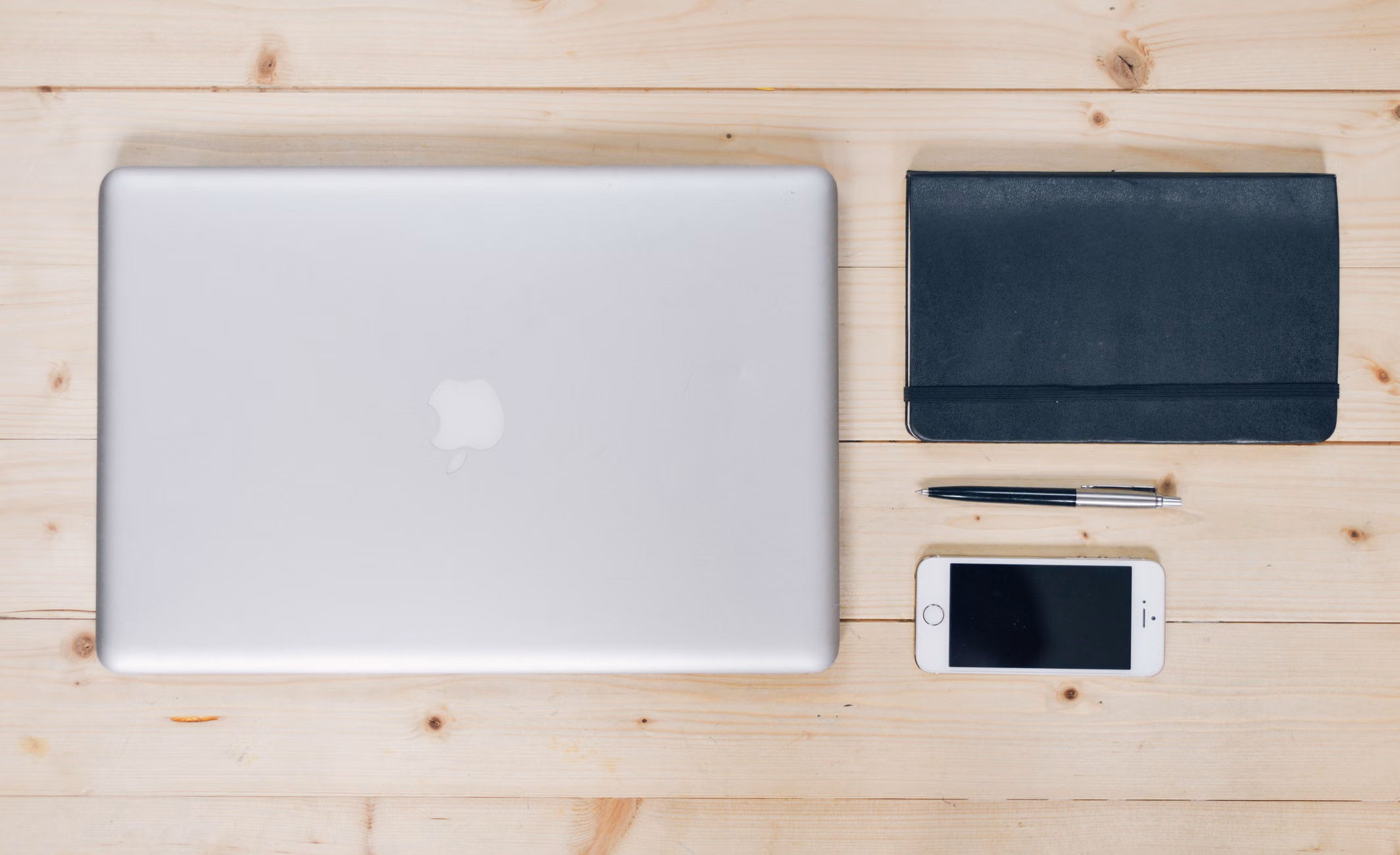 A clean, organized desk featuring a laptop, smartphone, notebook, and pen, ideal for productivity.