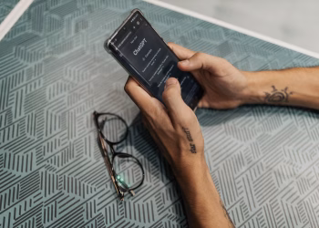 Close-up of a person holding a smartphone showing the ChatGPT app next to eyeglasses.