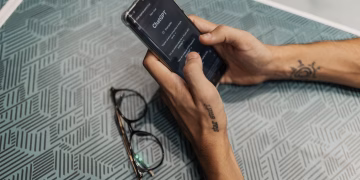 Close-up of a person holding a smartphone showing the ChatGPT app next to eyeglasses.
