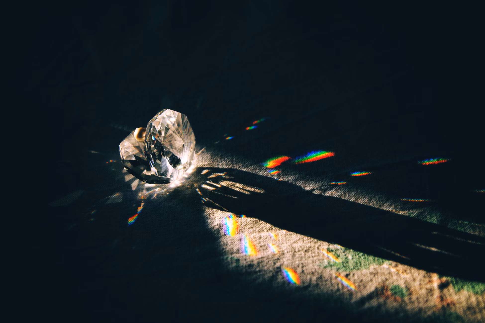 A diamond-shaped crystal casting rainbow reflections on a surface with dramatic lighting.