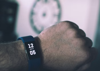 Close-up of a digital smartwatch showing time and date on a man's wrist indoors.