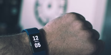 Close-up of a digital smartwatch showing time and date on a man's wrist indoors.