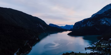 A breathtaking aerial view of Lake Molveno in Italy surrounded by mountains at twilight.